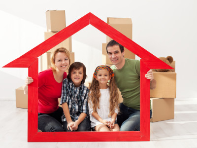 Image of family of four, smiling. holding red house frame.